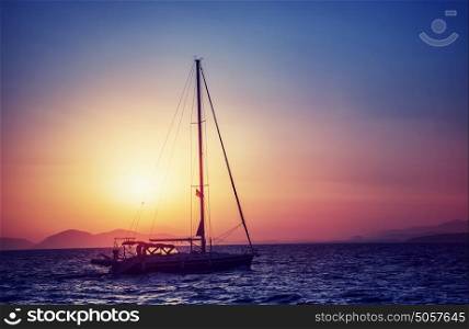 Silhouette of sailboat on sunset, water transport in bright yellow sun light, sea trip in the evening, traveling around Greek islands