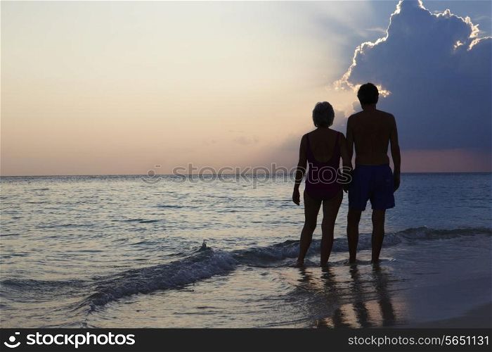 Silhouette Of Senior Couple Walking Along Beach At Sunset