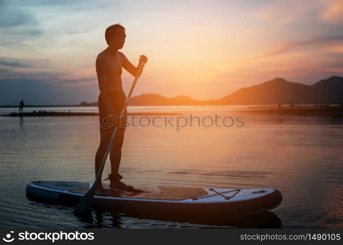 Silhouette of stand up paddle boarder paddling at sunset on a flat warm quiet river.