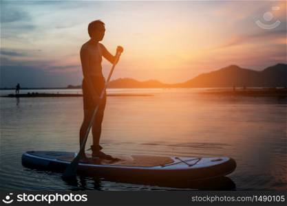 Silhouette of stand up paddle boarder paddling at sunset on a flat warm quiet river.