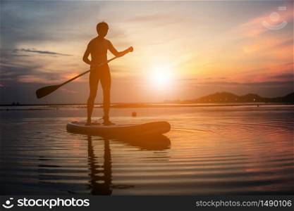 Silhouette of stand up paddle boarder paddling at sunset on a flat warm quiet river.