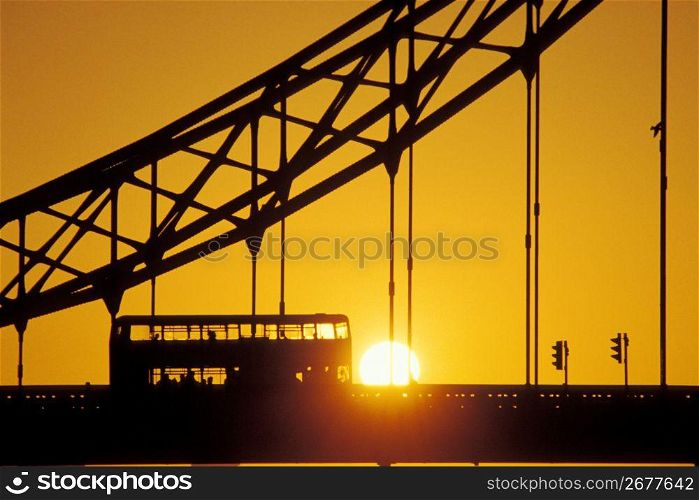 Silhouette of suspension bridge and double decker bus with sunset in background