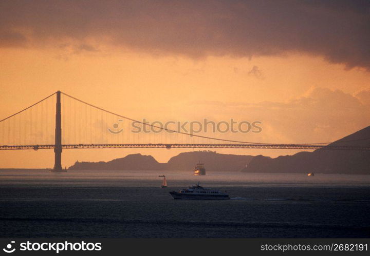 Silhouette of suspension bridge with boats in foreground