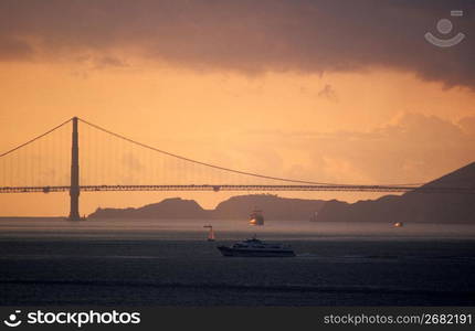 Silhouette of suspension bridge with boats in foreground