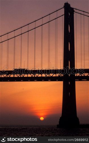Silhouette of suspension bridge with orange sunset in background