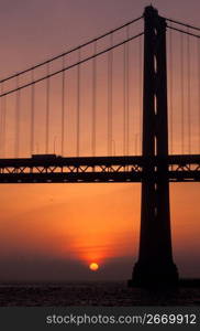 Silhouette of suspension bridge with orange sunset in background