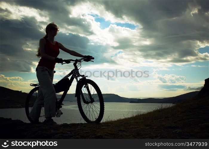 Silhouette of the girl with a bicycle against mountains