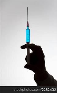 Silhouette of the hand of a female doctor with syringe filled with blue liquid. Vaccination concept.. Silhouette of the hand of a doctor with syringe filled with blue liquid. Vaccination concept.