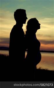 Silhouette of the man hugging his pregnant girlfriend
