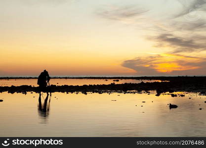 Silhouette of the photographer looking to the viewfinder on camera to capture the sunset in the evening at Pakarang beach, Phang Nga, Thailand