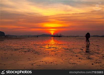 Silhouette of the photographer looking to the viewfinder on camera to capture the sunrise in the morning at Takua Thung, Phang Nga, Thailand