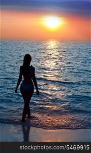 Silhouette of the sexual woman going at ocean towards to a sunset