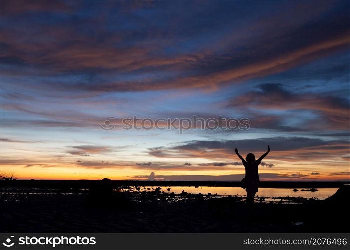 Silhouette of the woman raise her hand in the evening at Pakarang beach, Phang Nga, Thailand