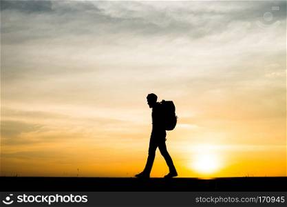 Silhouette of the young backpacker man walking during sunset.