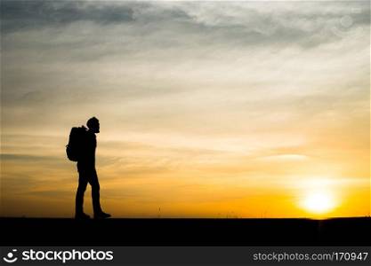 Silhouette of the young backpacker man walking  during sunset.