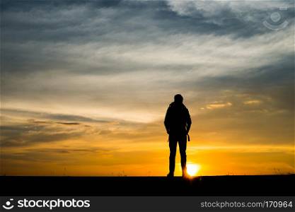 Silhouette of the young backpacker man walking during sunset.