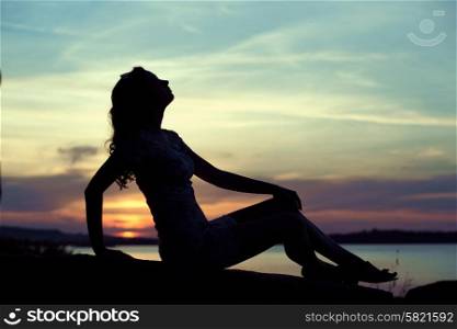Silhouette of the young lady sitting close to the sea
