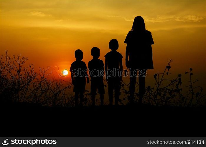 Silhouette of three children and mom standing at sunset. There is a mountain in the background.