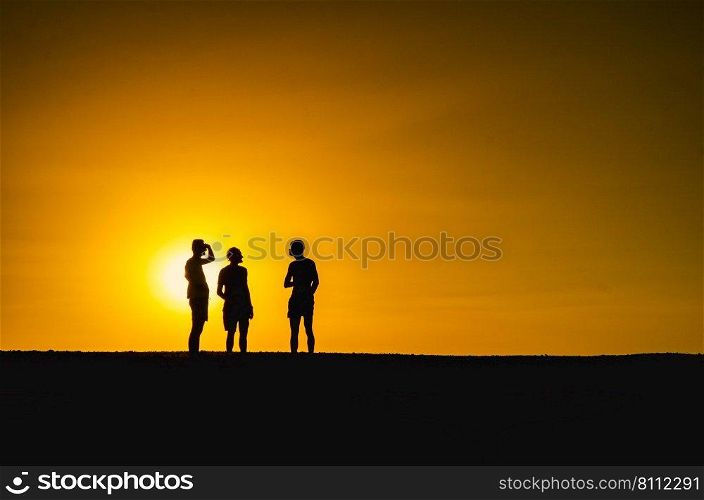 Silhouette of three persons with the sun falling in the background. Silhouette of three persons in an orange background