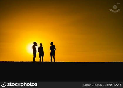 Silhouette of three persons with the sun falling in the background. Silhouette of three persons in an orange background