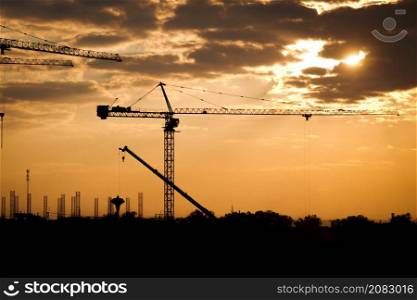 Silhouette of tower crane and large buildings construction site at sunset in evening time. New construction site with cranes on sunset background.