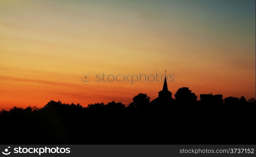 Silhouette of trees and church against a bright dawn sky