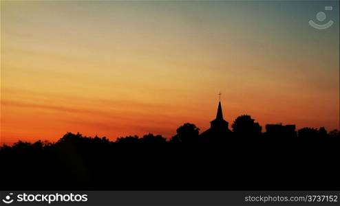 Silhouette of trees and church against a bright dawn sky