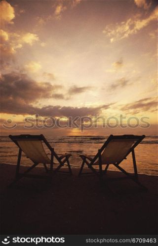Silhouette of two deck chairs at the beach during sunset