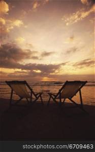 Silhouette of two deck chairs at the beach during sunset