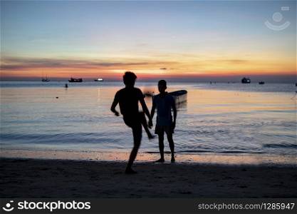 silhouette of two man playing football on sea beach against sunset sky
