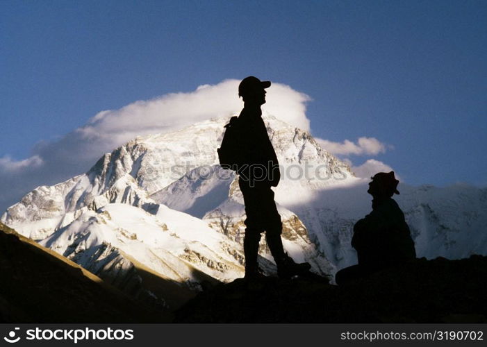 Silhouette of two men on a mountain with snow covered mountains in the background, Mt Everest, Tibet, China