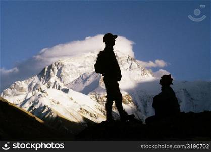 Silhouette of two men on a mountain with snow covered mountains in the background, Mt Everest, Tibet, China