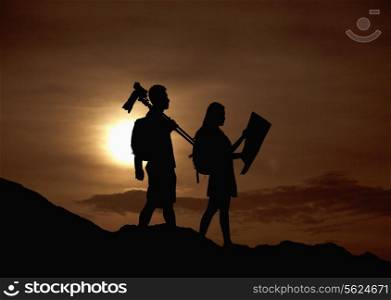 Silhouette of two people hiking and carrying camera and a map in nature at sunset