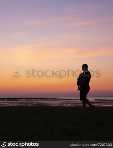 silhouette of walking father with child in belly carrier against colorful sunset