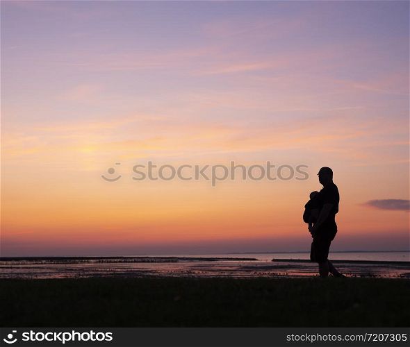 silhouette of walking father with child in belly carrier against colorful sunset
