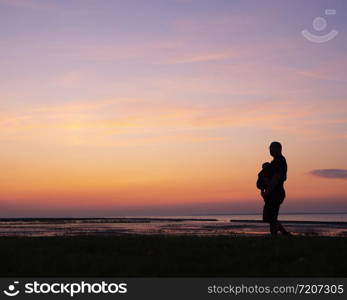 silhouette of walking father with child in belly carrier against colorful sunset