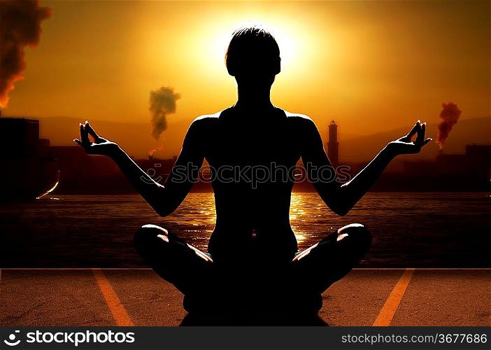 silhouette of woman in a sunset relaxing her mind with yoga near sea port with industry