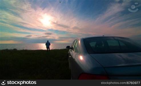 Silhouette of woman near his car enjoying view of the sea coast at sunset