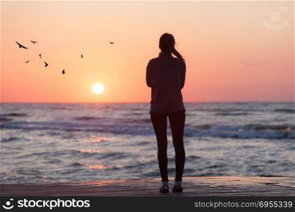 Silhouette of woman watching sunrise over ocean horizon