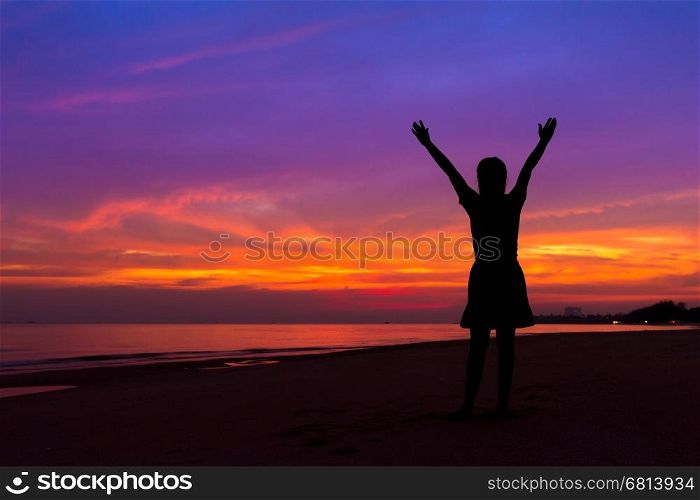 Silhouette of woman with hands up while standing on the sea beach at sunset