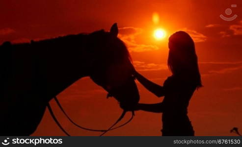 Silhouette of young girl rider with horse against sun and dramatic sky