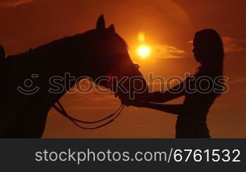 Silhouette of young girl rider with horse against sun and dramatic sky