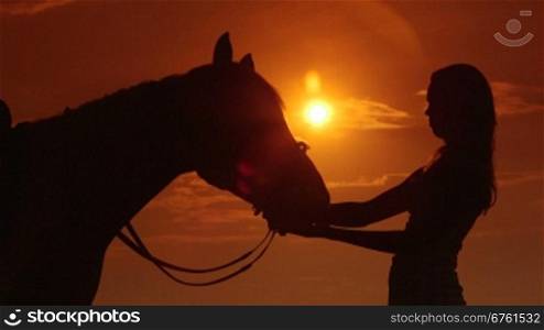 Silhouette of young girl rider with horse against sun and dramatic sky