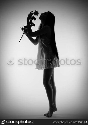 Silhouette of young girl with rose flower on gray background (monochrome)