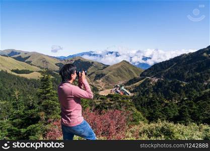 Silhouette of young man in pink long sleeved t-shirt enjoying the amazing view and take a photo on top of mountain