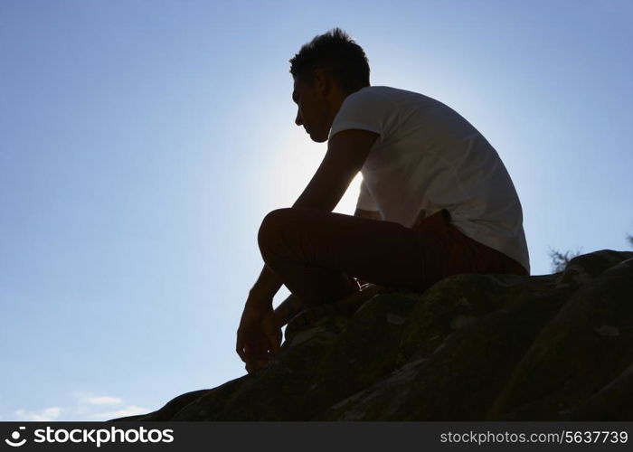 Silhouette Of Young Man Sitting On Rock
