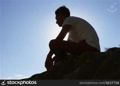 Silhouette Of Young Man Sitting On Rock