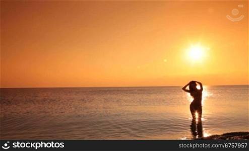 silhouette of young woman in a bikini coming out of the sea at sunset