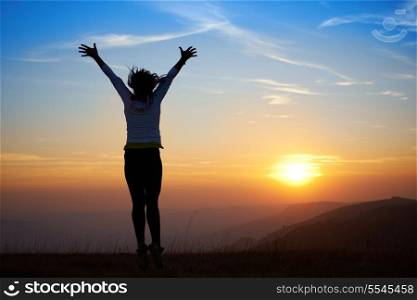 Silhouette of young woman jumping against sunset