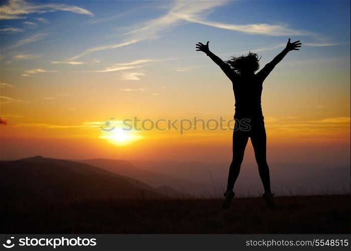Silhouette of young woman jumping against sunset with blue sky